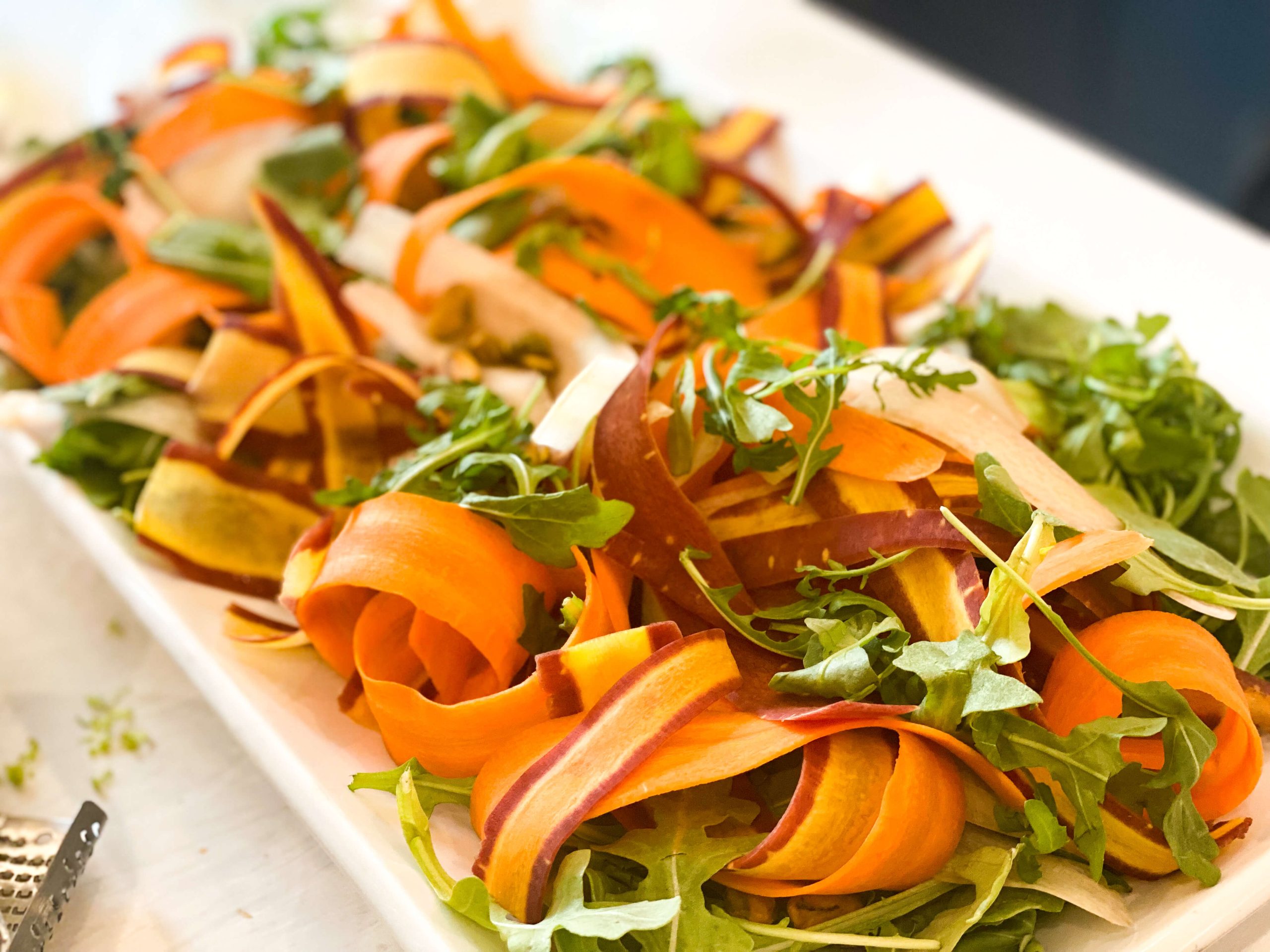 Salad on serving platter with carrot ribbons and arugula