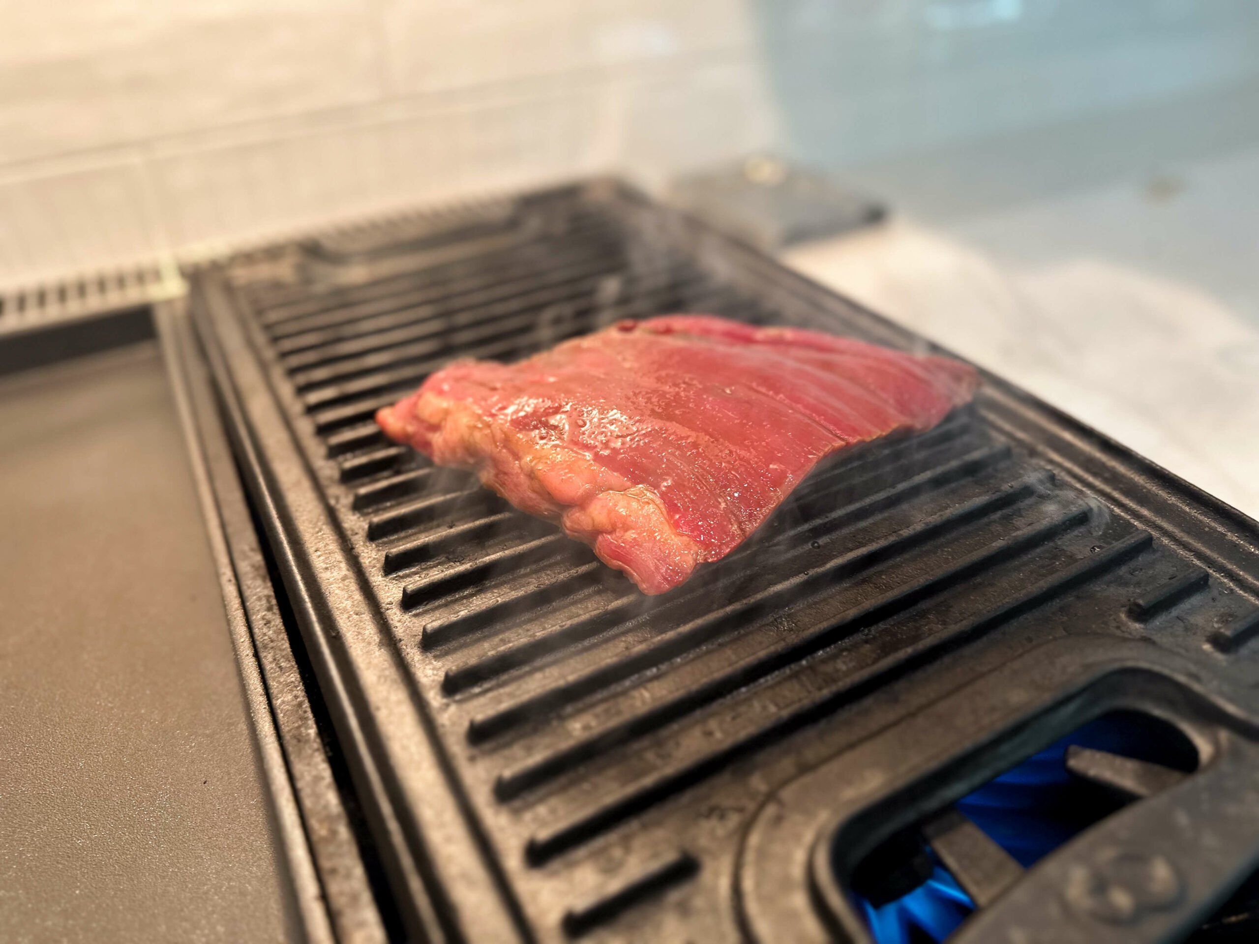 flank steak cooking on hot grill