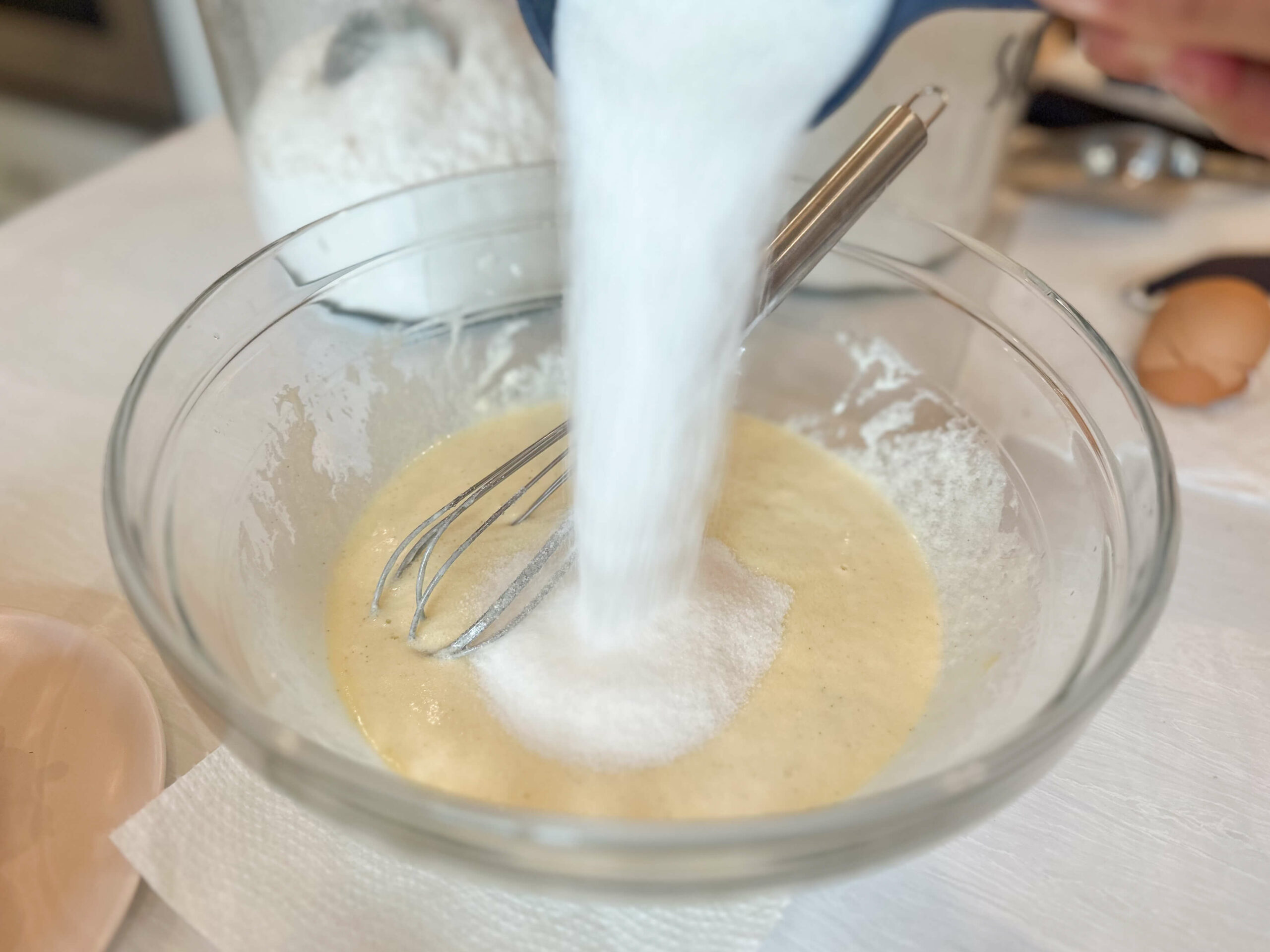 sugar being poured over wet ingredients in large bowl. 