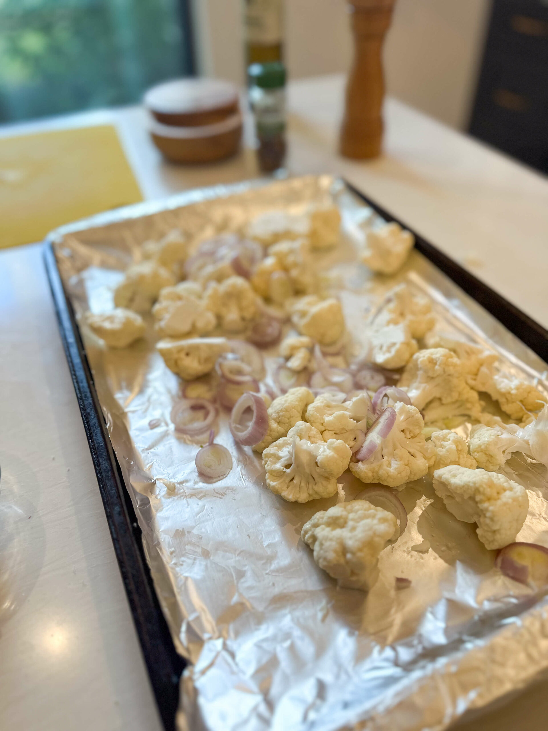 cauliflower in lined baking sheet with sliced shallots
